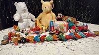 Photo showing two stuffed bears, one white plush with sparkly details and one yellow teddy bear, along with assorted small vintage toys including colorful wooden fish and plastic toys.