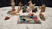 Photo of the full collection spread on a lace tablecloth showing a variety of handcrafted animals, figurines, and a textile piece.