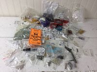 Wide view of multiple jewelry findings and beads, most in plastic bags, arranged on table with orange lot label in center.