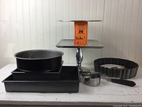 Lot overview photo displaying metal cake stands, rectangular and round cake pans, tart pan, and measuring spoons