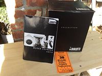 Photo of the Bialetti Mukka Express Vetro manual and black product box on a wooden surface.