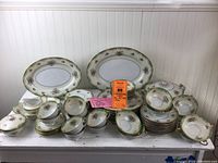 Full display of the china set including platters, plates, cups, saucers, serving bowls, and tureen, displaying the overall pattern and quantity