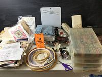 Overview of the embroidery lot showing floss, hoops, kits, pattern sheets, fabric, scissors, and accessories arranged on a table.