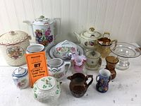 Full view of the collection showing a variety of vintage china with floral and gold details, pink ruffled vase and brown pitchered items