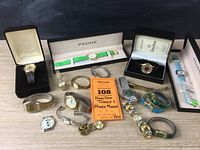 Full view of 12 watches on table with some in boxes and an auction label showing seller's description and lot number.