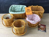 All five Longaberger baskets arranged on wooden surface against black backdrop showing fabric liners, handles, and glass inserts.