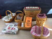 Wide shot of all six Longaberger baskets with various fabric liners and lids, arranged on a wooden surface under natural light.