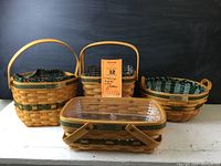 Four Longaberger baskets with cloth and plastic liners arranged together. A tag with item number and collection details is placed behind the baskets.