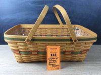 Full side view of the basket showing its rectangular shape, woven pattern, red and green accents, and two attached wooden handles.