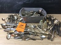 Wide view of mixed silverplate and sterling flatware with forks, spoons, knives in a bin and spread out