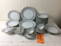 Full view of the Noritake China Sabrina pattern dinnerware set including stacks of plates, bowls, cups with saucers, and additional serving pieces arranged on white surface.