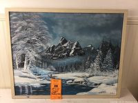 Full view of framed canvas painting depicting a winter snow landscape with river and mountains, showing overall artwork and frame.