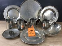 Photo showing the full collection of large and medium round pewter plates, four pitchers, candlestick holder, and bowl grouped on a table.