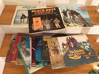 Photo of multiple vinyl record albums including The Beatles Yellow Submarine and several Beach Boys albums laid out on a wooden surface.