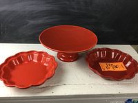 Photo showing the red ceramic pedestal fruit bowl in the center with two red ceramic fluted pie plates on each side.