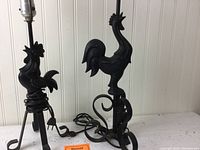 Side view of the two black metal rooster lamps displaying electrical wiring and rooster sculptural design.