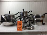 Group photo showing nine Farberware pans and lids arranged on a white surface showing handles, lids, and cookware bodies.
