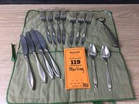 Full set of utensils arranged on green cloth: 5 knives, 7 forks, 2 spoons, bottle opener