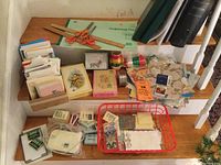 Overview of vintage greeting cards, gift wrap rolls, ribbons, scissors, rulers, and other stationery items stored on a staircase and table.