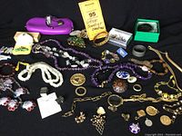 Full collection of vintage jewelry laid out on black surface showing various necklaces, brooches, bracelets, pins, and charms.