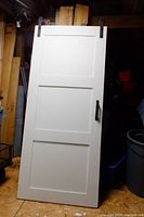 Full view of one white three-panel interior barn door with black handle and top-mounted black sliding hardware.