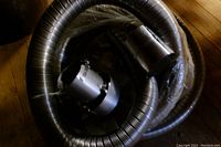 Coiled flexible stainless steel chimney liner with attached coupling and rain cap, coiled on wooden floor.