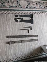 Two complete sets of antique barn door hinges and matching latch hardware laid out on a patterned carpet surface.