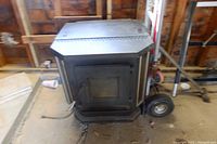 Front view of black pellet stove in unfinished shed with glass door and power cord