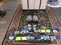 Pair of Rossignol skis with blue, green, and yellow graphics and attached white and blue bindings, placed on a patterned rug.
