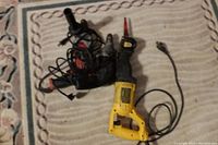 Top view of three power tools: yellow Dewalt reciprocating saw, black and red hammer drill, and Craftsman drill on carpeted floor.