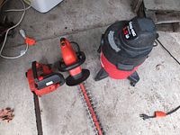 Overview of all three items together on concrete floor: Homelite chainsaw, Black & Decker electric hedge trimmer, and Shop-Vac wet/dry vacuum.