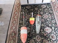 Three vintage lobster buoys placed on a patterned carpet showing different designs: striped wooden buoy, yellow-red buoy with handle, and metallic buoy.