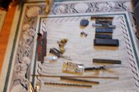 Blurry photo showing various small vintage tools laid out on a decorative carpet, including knives, oil stones, and bits.