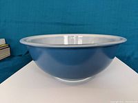 Side profile view showing the smooth curved shape and blue exterior with white interior of the Pyrex bowl.