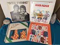 Four comedy vinyl albums arranged side by side against a wall, showing cover artwork and titles