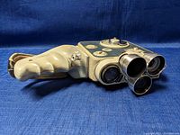 Vintage Eumig C3M movie camera laying on blue fabric. Shows camera body, ergonomic grip, and front lenses.