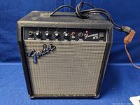 Front view of Fender Frontman 15B amplifier showing control panel, including input, volume, tone controls, aux in, headphones jack, and power switch. Fender logo visible on speaker grille.