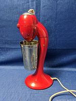 Side view of red Hamilton Beach milkshake mixer with attached stainless steel cup, showing power cord and classic design.