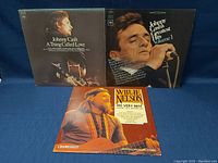 Three vinyl albums: Johnny Cash 'A Thing Called Love', Johnny Cash 'Greatest Hits Volume 1', and Willie Nelson 'His Very Best (1962-1973)' displayed upright showing cover artwork.