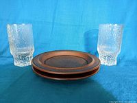 Two Littala 'Aslak' juice glasses and two Arabia Ruska plates arranged on blue cloth.