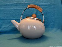 Side view of the grey enamel kettle with wooden handle on upper bail and lid knob.