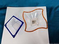 Top view of two glass dishes, orange-edged and blue-edged, placed on blue fabric background
