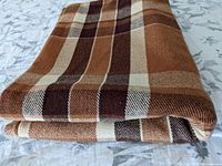 Folded view of the blanket showing its thick wool texture and plaid pattern in browns, cream, and tan.