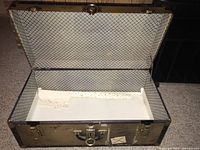 Open antique trunk showing patterned interior lining and wear on lining paper.