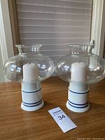 Pair of candle holders with glass globes on wooden surface, white candles inside, ceramic bases with blue stripes.