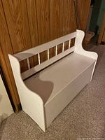 Front and side view of a white wooden child's bench with a spindle backrest, showing one armrest designed to hold a wine bottle.