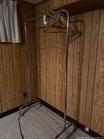 Full view of the metal rolling clothing rack with several wooden and wire hangers attached