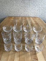 Top-down view of 16 glasses arranged on wooden table showing clearness and cut glass patterns of the crystal glasses.