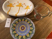 Photo showing all three items: the oval platter with giraffe design, the glass measuring cup, and the round handpainted plate with detailed patterns