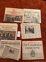 Five Canadian newspaper sections from the early 1980s covering constitutional events and Toronto's history spread on an orange carpet.